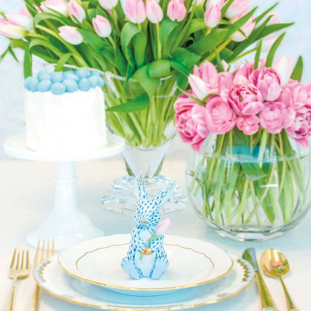 Blue-and-white Herend bunny at a gold-rimmed place setting with pink tulips, crystal, and gold flatware
